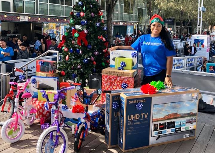 A woman stands in front of Christmas tree surrounded by presents at Discovery Green in downtown Houston