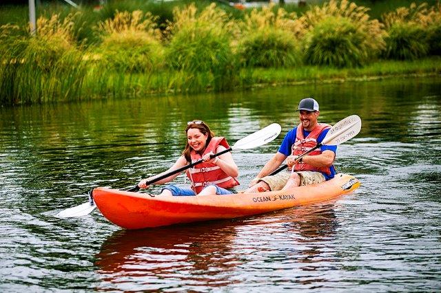 A couple is seen rowing an orange kayak on Kinder Lake in Discovery Green