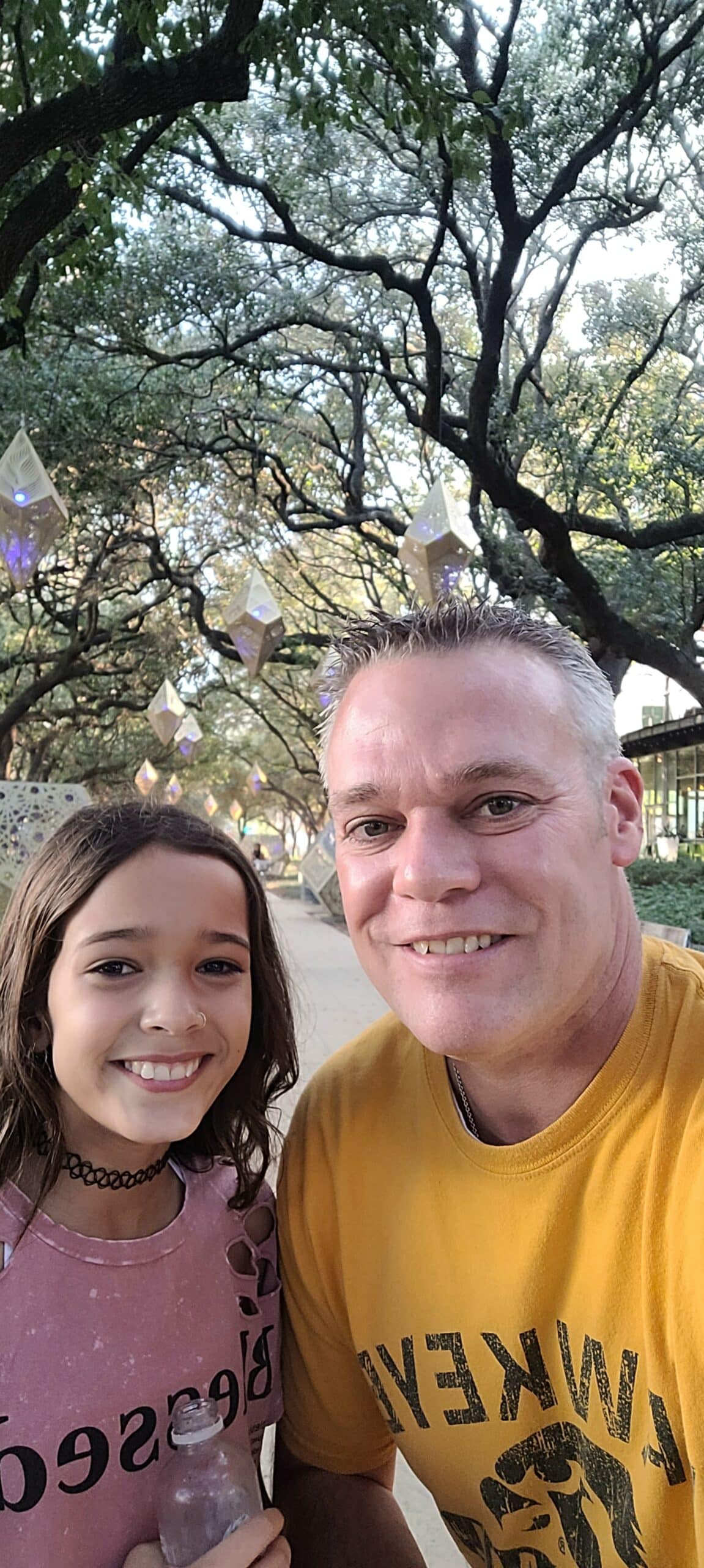 A dad and a daughter take a selfie under the oak trees at Discovery Green