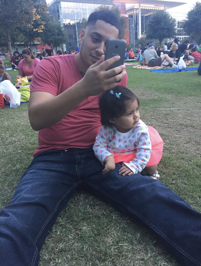 A man and his daughter sit on the performance lawn at Discovery Green