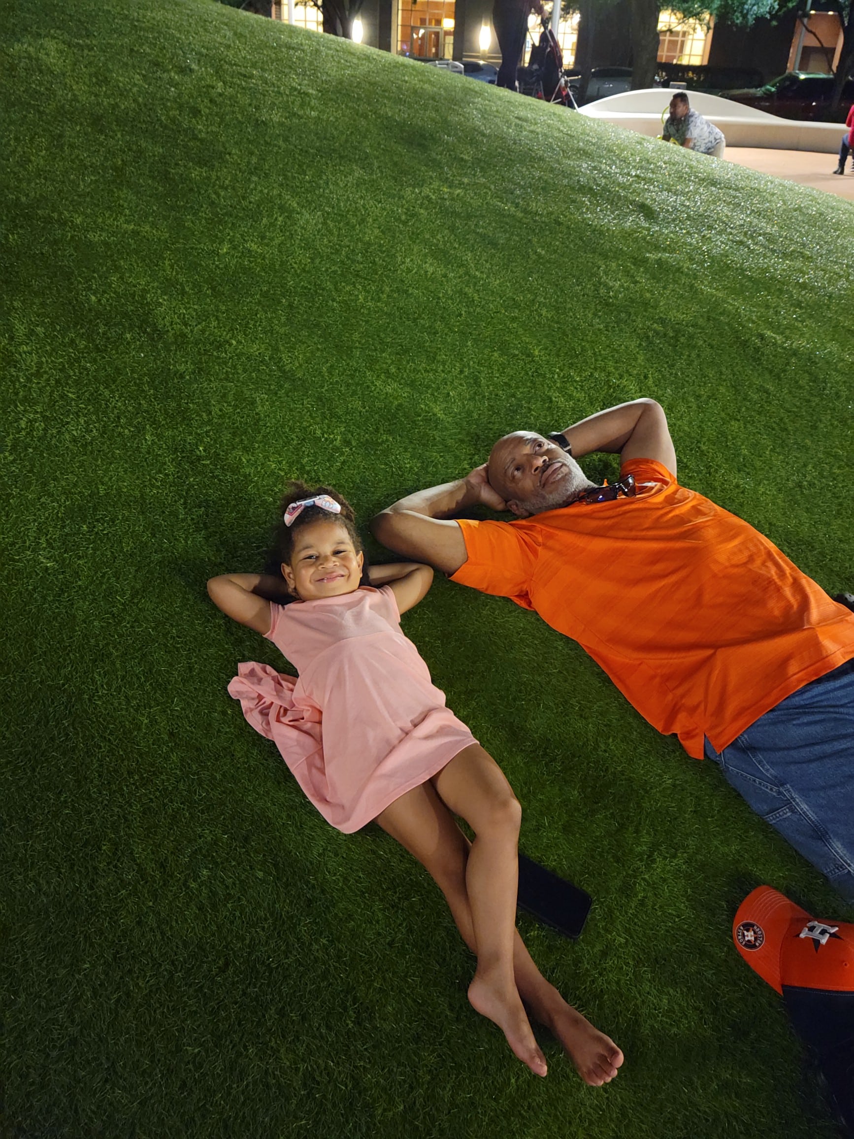 A man and a girl lay back on the hill in the playground at Discovery Green