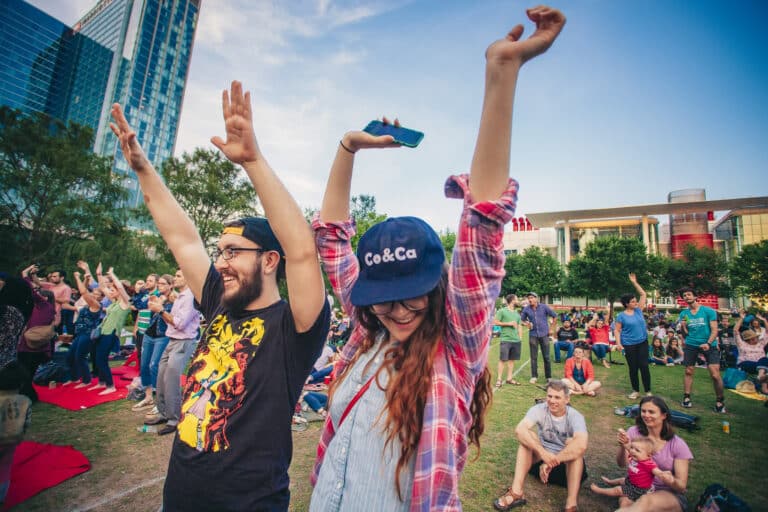 People are seen throwing their hands up and dancing at a concert at Discovery Green in Downtown Houston.
