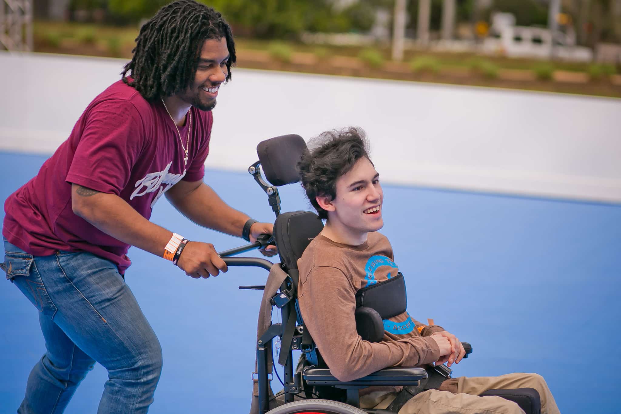 A man on roller skates pushes a friend in a wheelchair at The Rink: Rolling at Discovery Green in downtown Houston